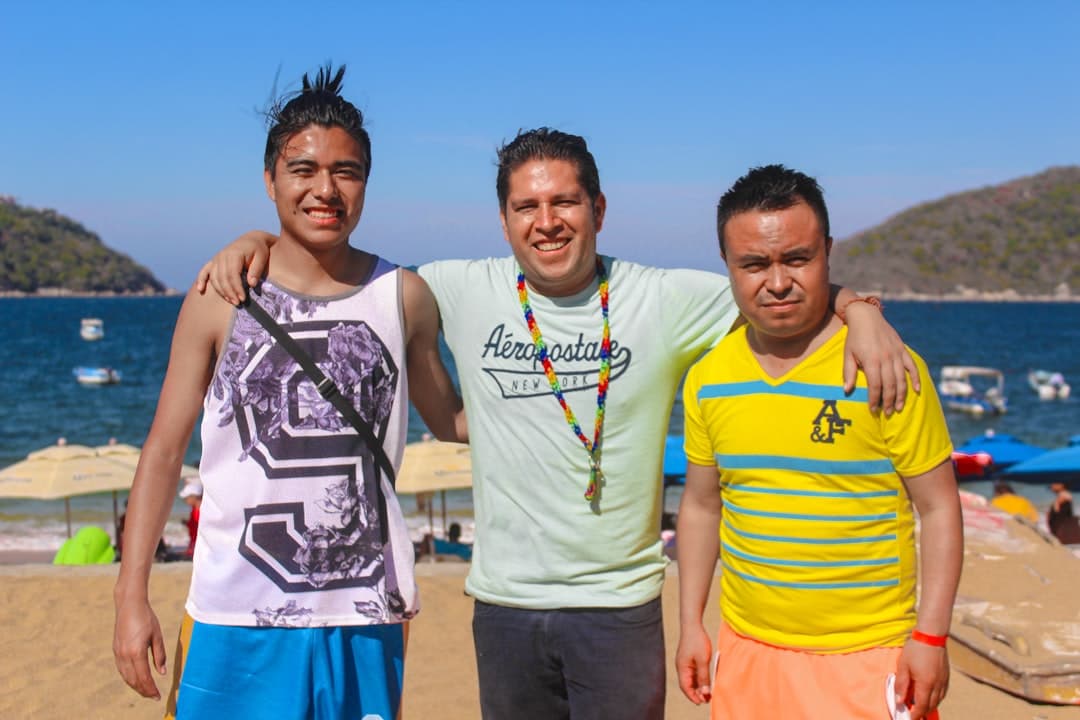 Three friends pose together on a sunny beach.