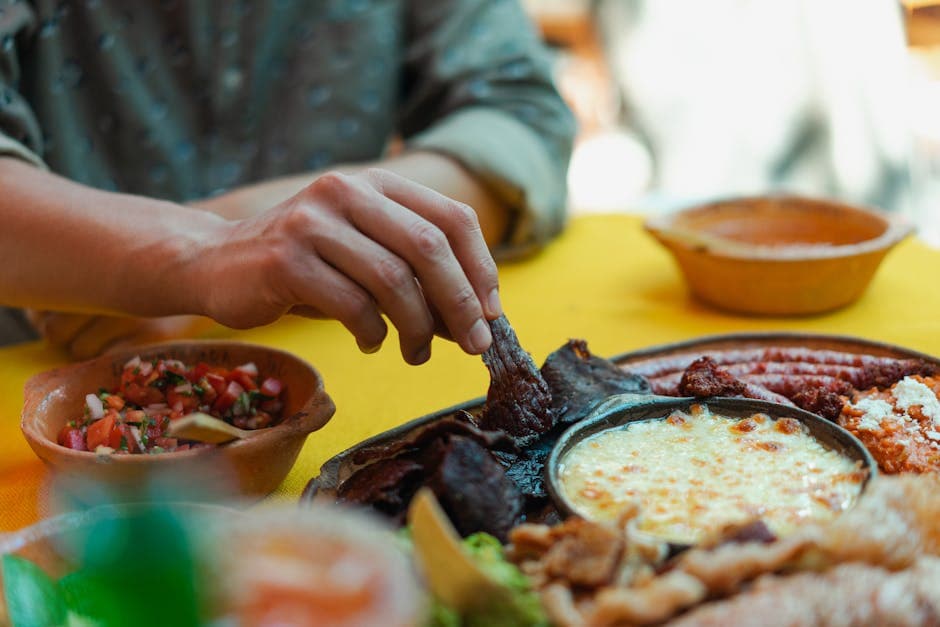 A hand enjoys traditional Mexican cuisine with cheese and salsa on a vibrant table setting.