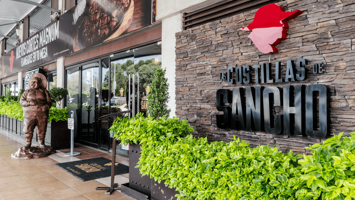 Exterior de Las Costillas de Sancho Ags Sur con su letrero iluminado y una mesa al aire libre mostrando una bandeja de costillas y papas