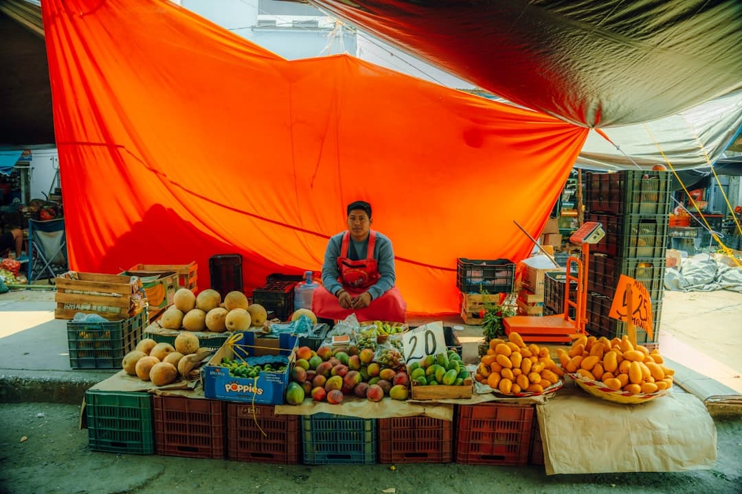 A fruit seller sits behind a colorful market stall.