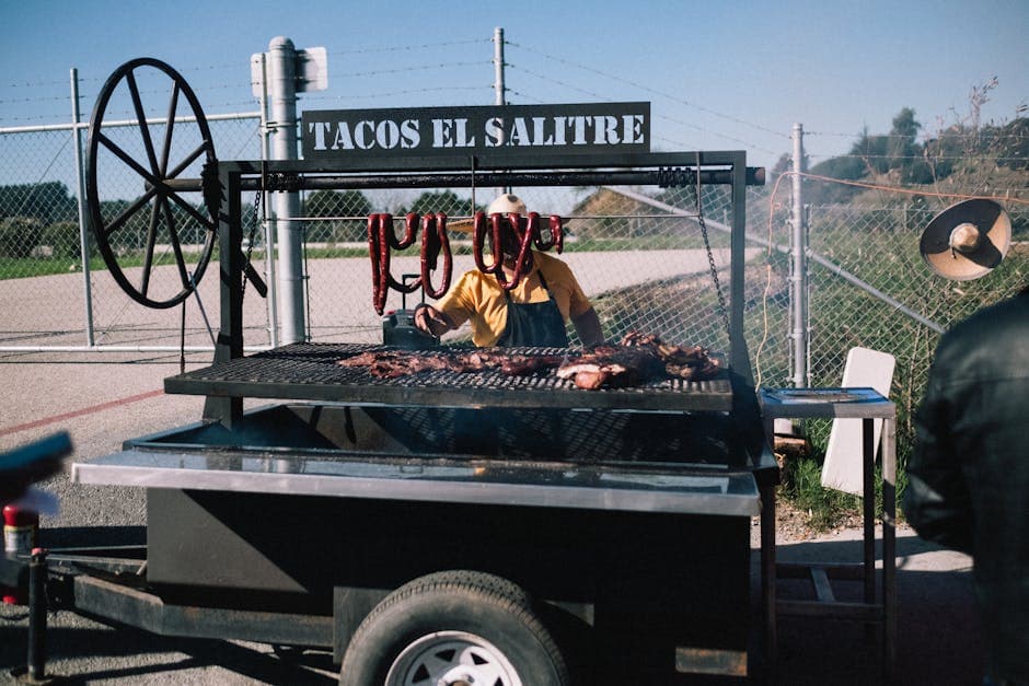 Street food vendor grilling meat at Tacos El Salitre stand on a sunny day.