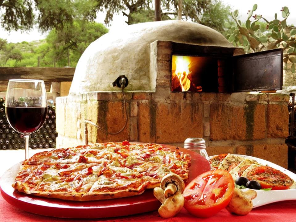 Armadilli Pizzeria — interior con horno de leña encendido y una pizza margarita recién salida, mesa de madera