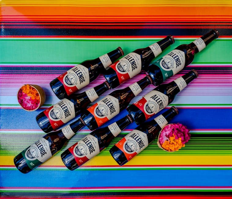 A vibrant display of Allende beer bottles on a colorful Mexican textile with flower petals.
