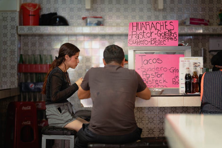 Two people sitting at a street food counter in Ciudad de México enjoying tacos.