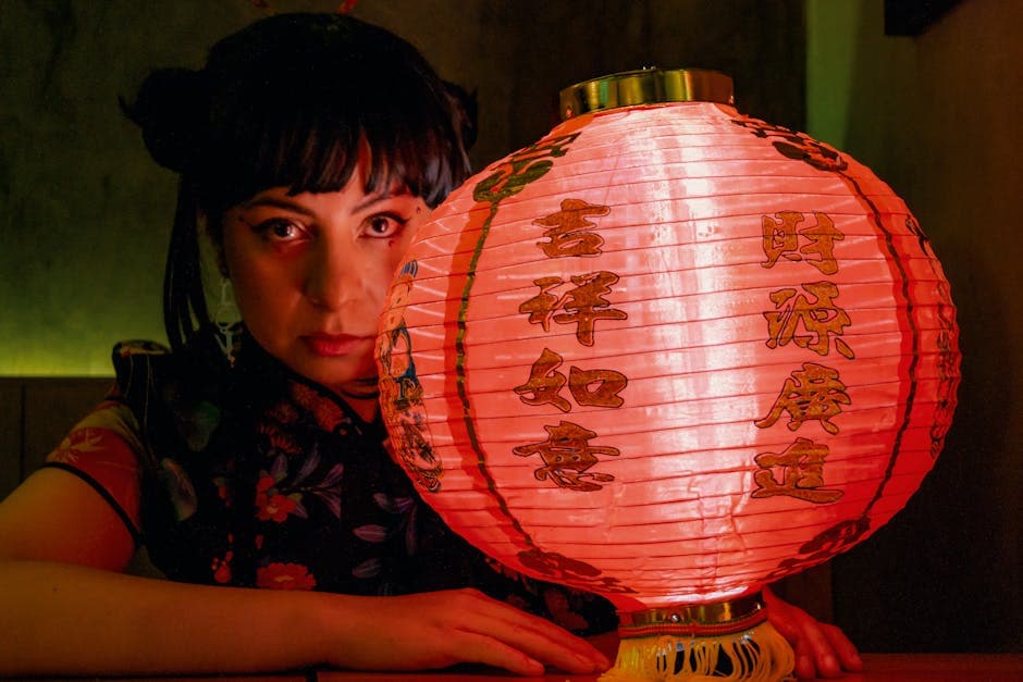 A woman holds a glowing red lantern with Chinese characters in a dimly lit room, creating a mysterious atmosphere.