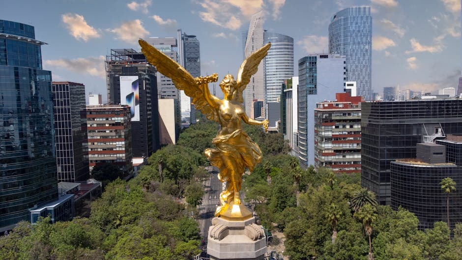 Aerial view of the Angel of Independence surrounded by modern skyscrapers in Mexico City.