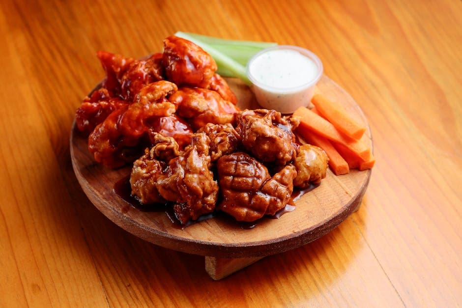 Tasty chicken wings served with vegetables and sauce on a wooden plate.