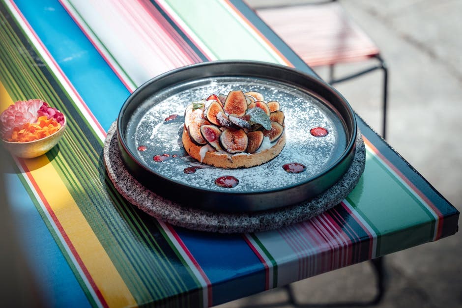 Delicious fruit tart garnished with figs and powdered sugar served on a colorful table in daylight.