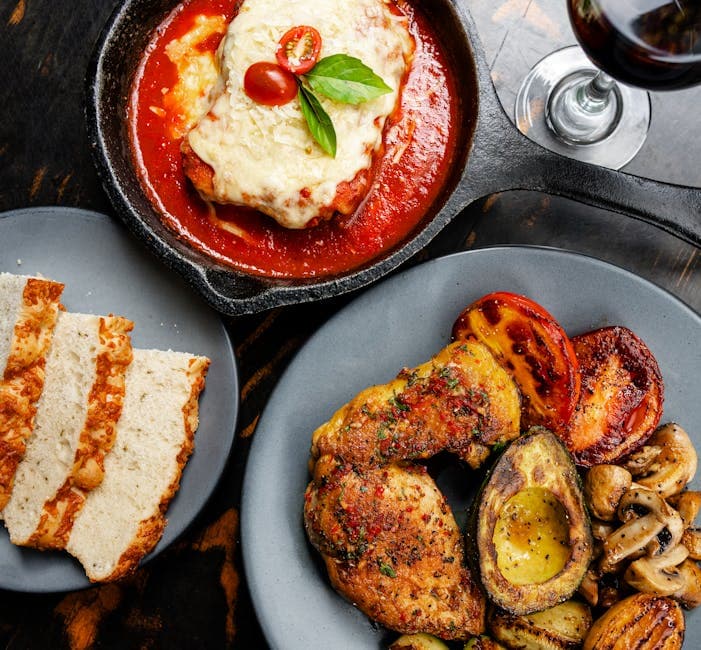 Top-down view of Chicken Parmesan with grilled vegetables and wine, a classic Italian dinner setting.