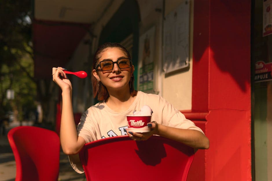 A woman in sunglasses enjoys a scoop of ice cream in the outdoor seating area. Captured on a sunny day.