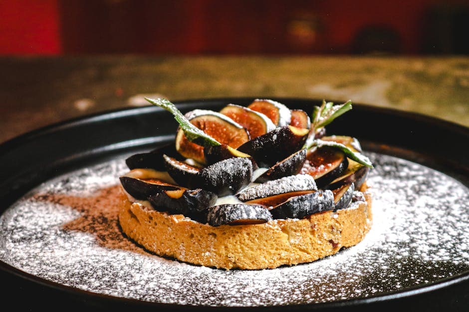 Delicious fig tart dusted with powdered sugar, served on a black plate, photographed in Ciudad de México.