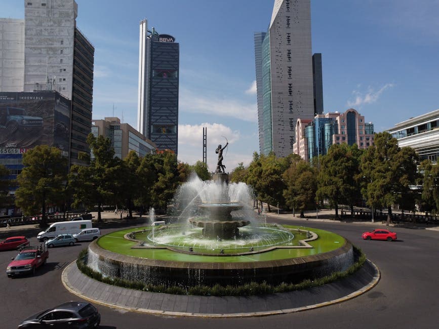 Scenic view of a roundabout featuring a central fountain surrounded by skyscrapers on a sunny day.