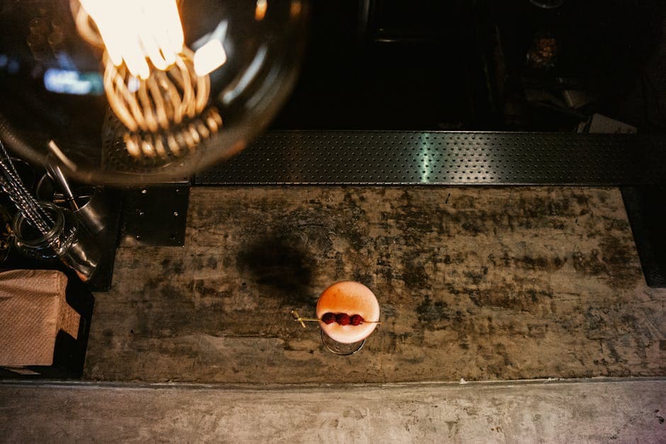 Stylish aerial view of a cocktail with raspberries on a rustic bar counter, illuminated by warm lighting.