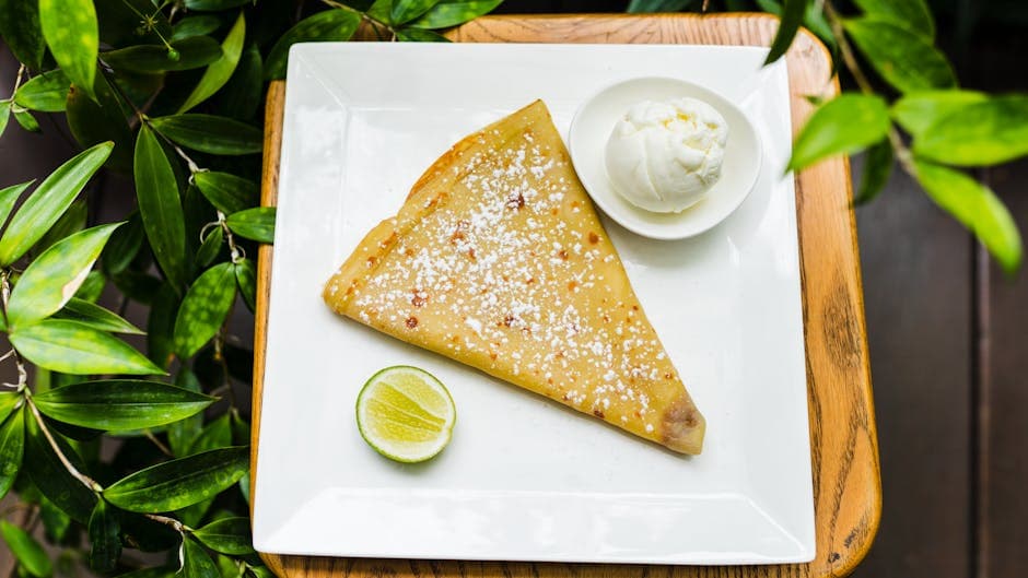 Crepe served with ice cream and a slice of lime on a square plate, viewed from above.