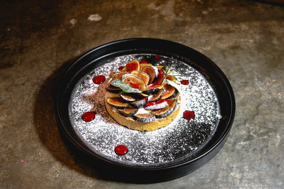 Close-up of a gourmet fig tart elegantly served on a black plate, dusted with powdered sugar.