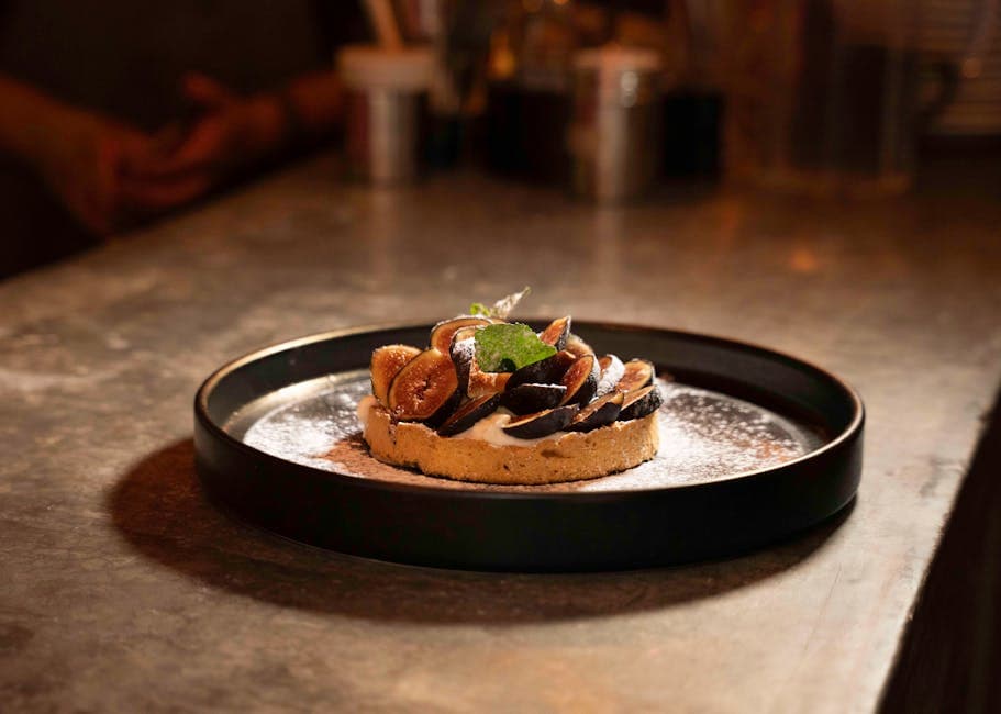 Artistic food photography of a fig tart dusted with powdered sugar on a black plate.