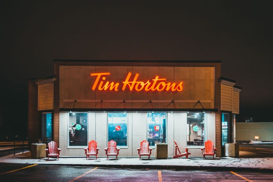 Modern fast food restaurant exterior with inscription above armchairs on walkway with snow in evening city