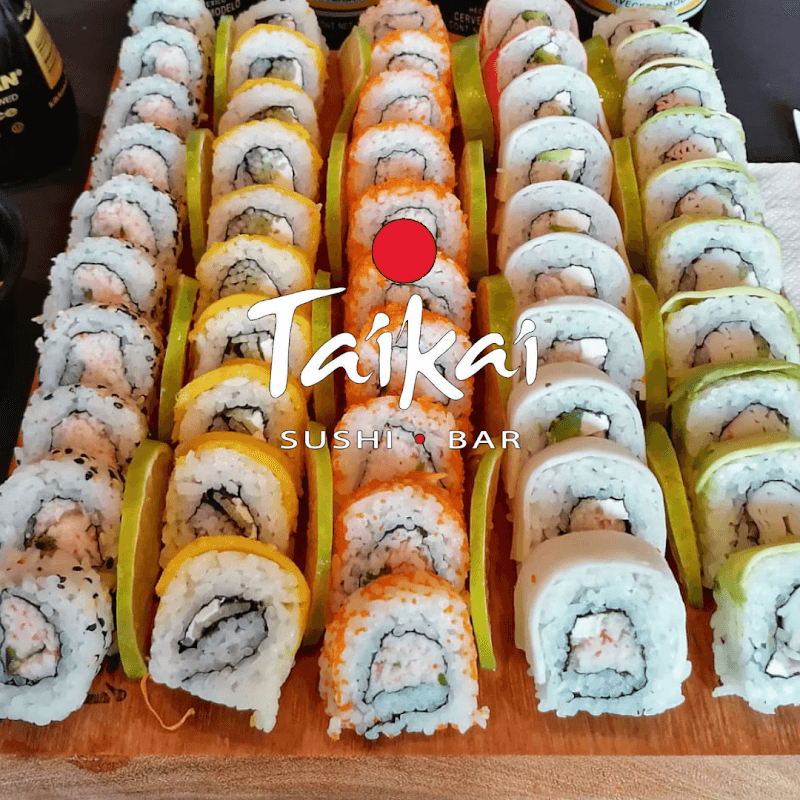 Taikai Victoria — fachada con letrero rojo y barra de sushi con rollos coloridos en la mesa
