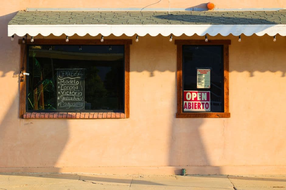 Facade of a local bar with an open sign in English and Spanish under warm sunlight.