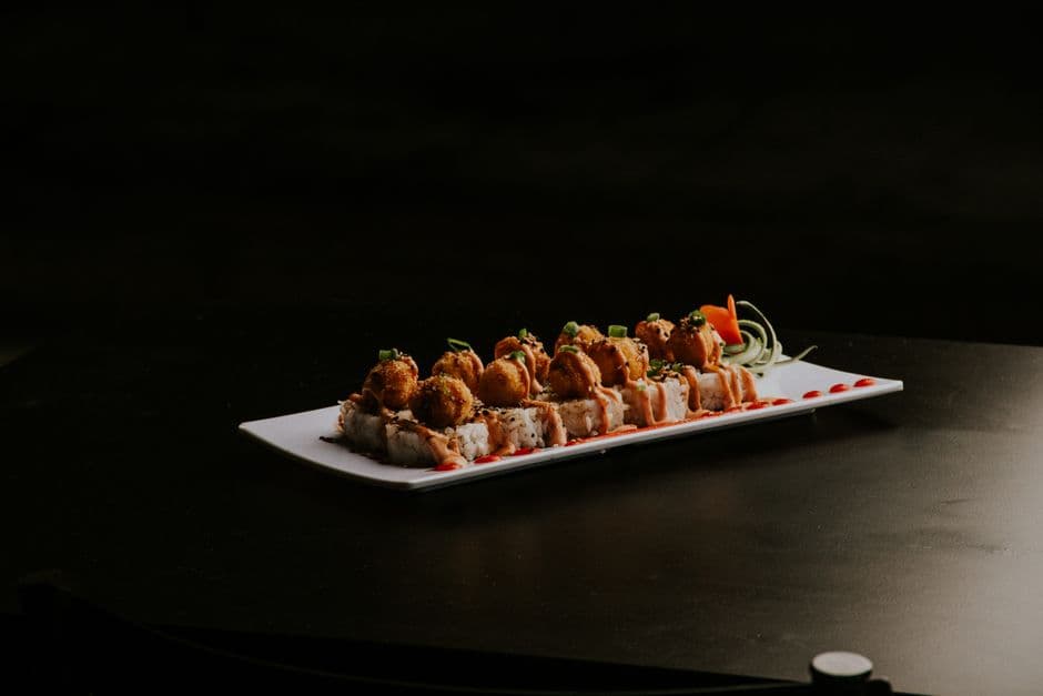 Gourmet sushi roll with crispy tempura topping, garnished with vegetables on a black background.