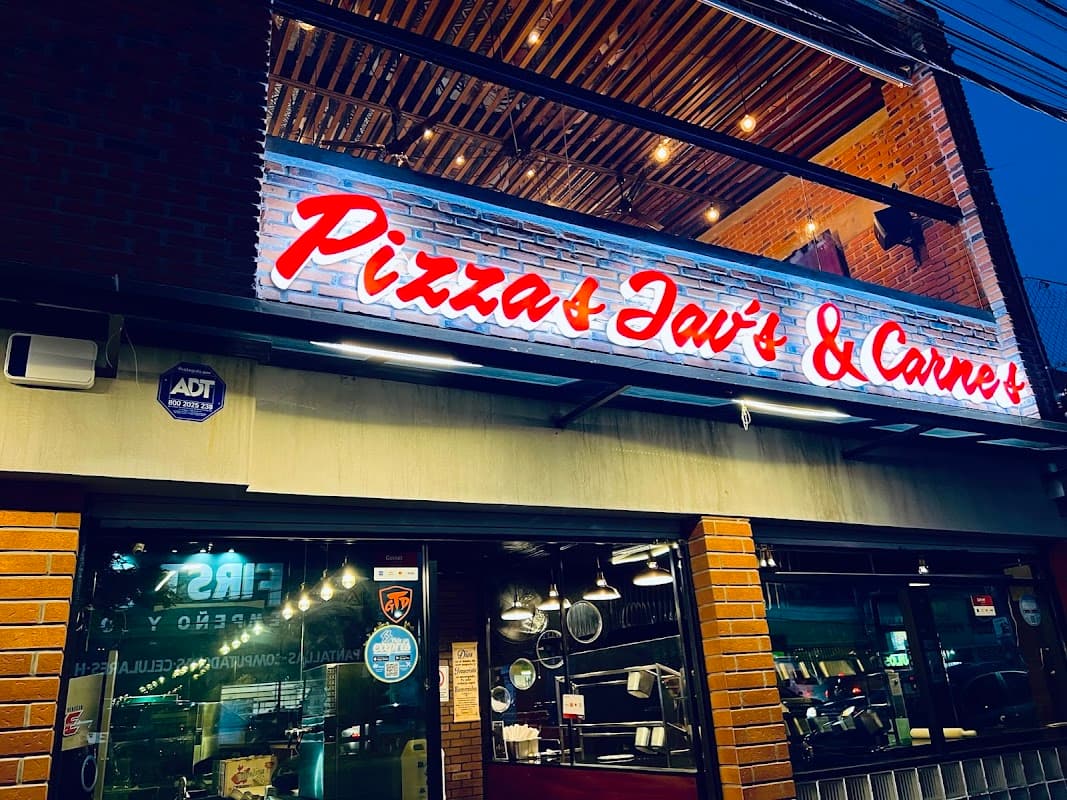 Pizzas Jav's - Sabor y Calidad, fachada iluminada y una pizza de arrachera en la mesa, mostrando la terraza al atardecer