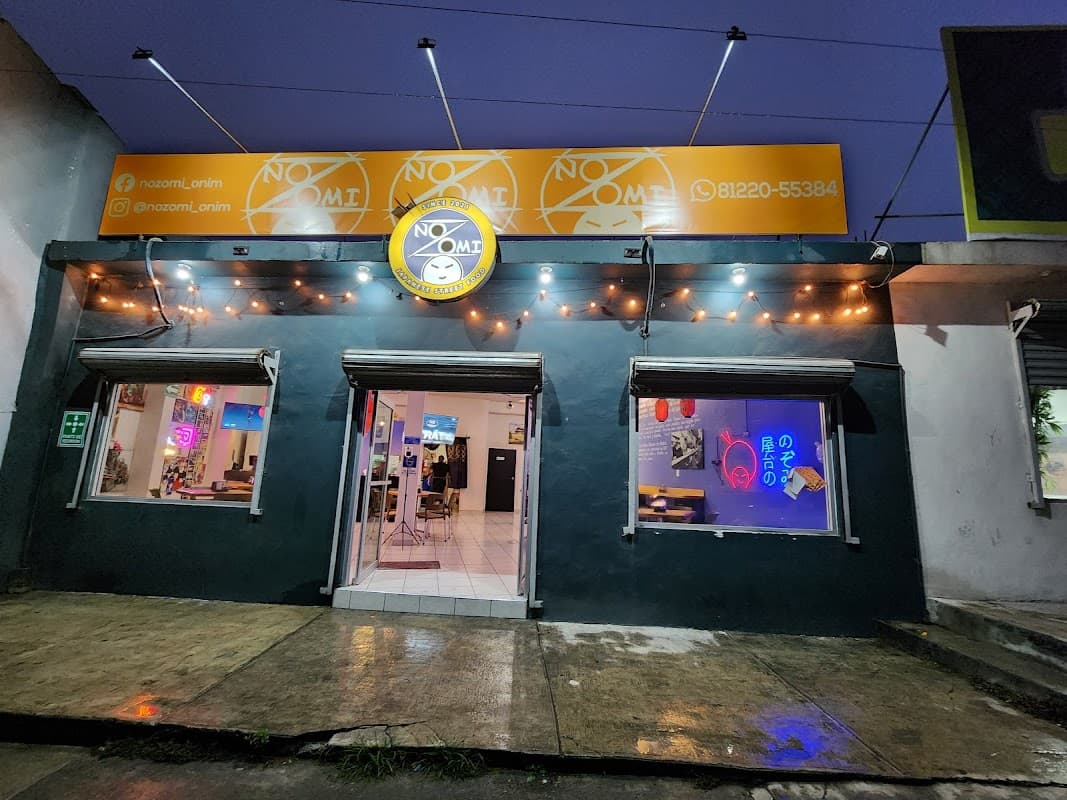 Fachada iluminada de EL TERRENO FOOD PARK con puestos de sushi y tacos al frente — vista exterior al atardecer