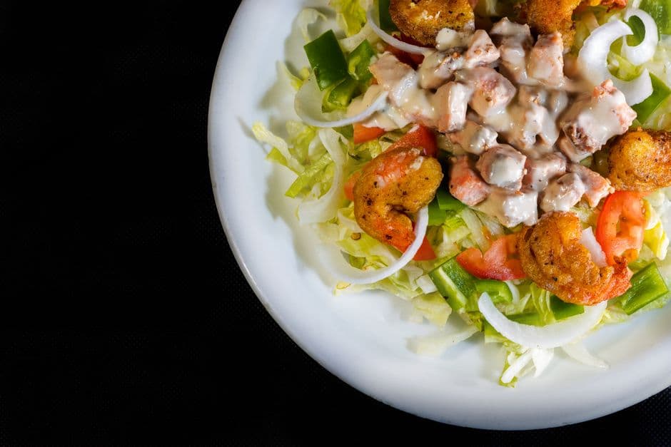 A vibrant shrimp salad on a white plate with fresh vegetables and creamy dressing, viewed from above.