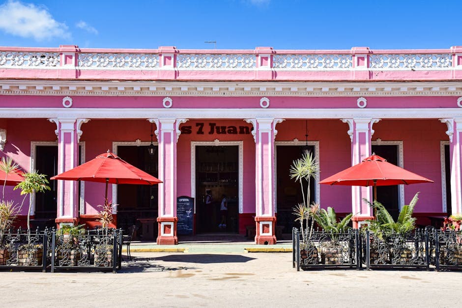 Sunlit pink café with red umbrellas in Remedios, Cuba, showcasing colorful colonial architecture.