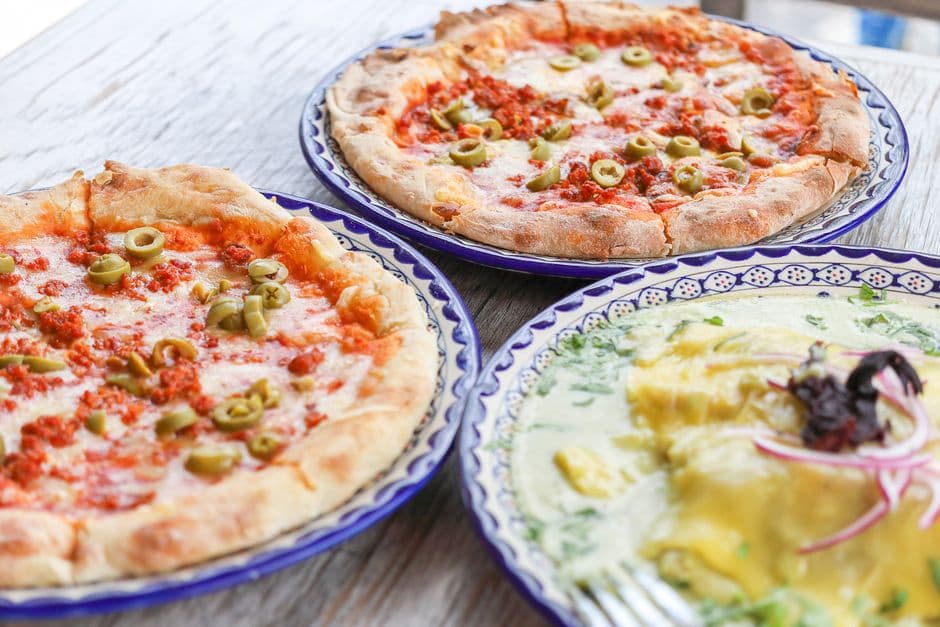 Freshly baked pizzas topped with mozzarella, olives, and sausage on a rustic table.