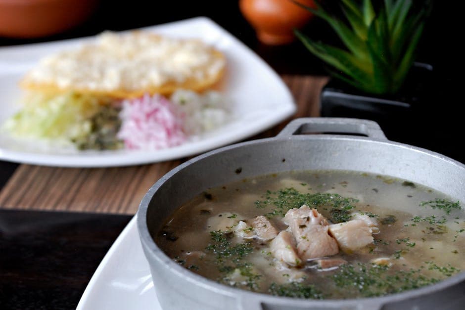 Delicious Mexican soup in a pot with sides of radish, lettuce, and crispy tortilla in a restaurant setting.