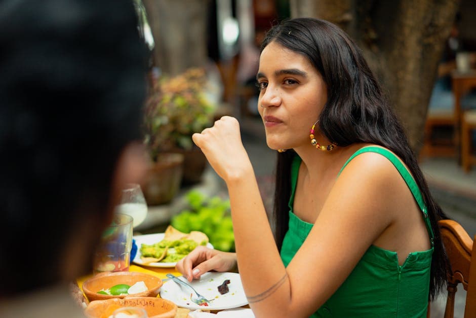 Young woman in green top dining outdoors, enjoying delicious Mexican food on a sunny day.