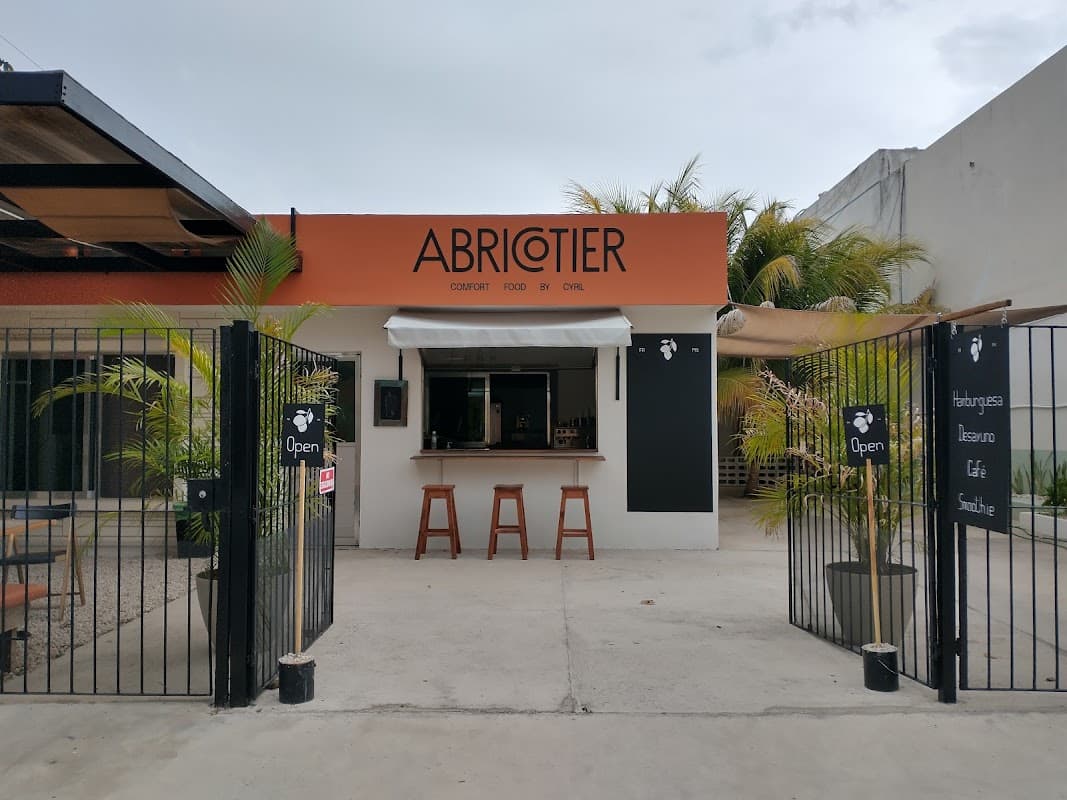 Vista exterior de Abricotier Hamburguesas en C. 23 131, mostrando el letrero y la terraza al atardecer
