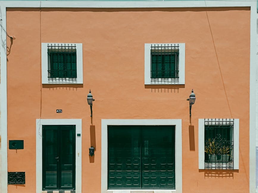 Vibrant orange facade of a house in Mérida, Mexico featuring decorative iron grilles on windows.