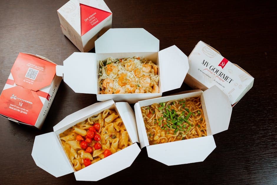 Three gourmet takeout meals in open boxes showcasing pasta and noodles.