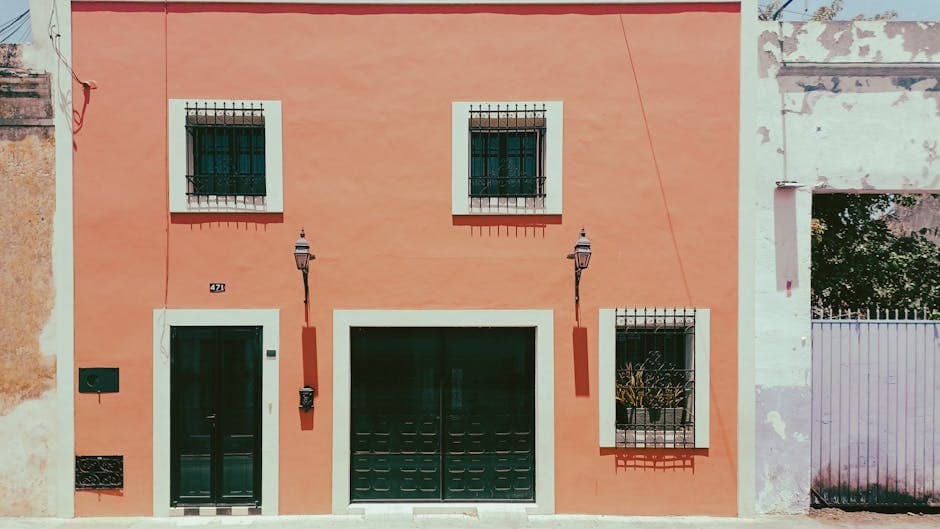 Vibrant coral-colored colonial house facade in Mérida, Yucatán with traditional iron shutters.