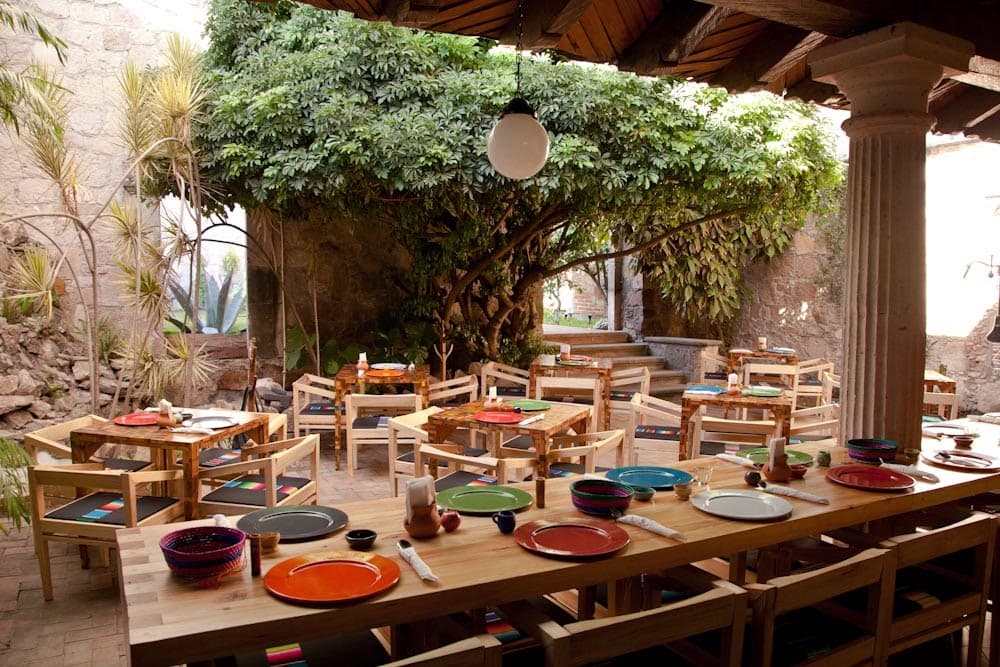 Tata Mezcalería + Cocina – interior con barra de mezcal, botellas iluminadas y mesas de madera