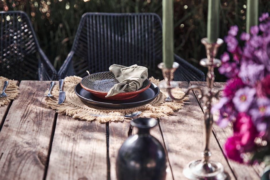 Rustic outdoor dining setup with elegant tableware, flowers, and greenery, perfect for special occasions.