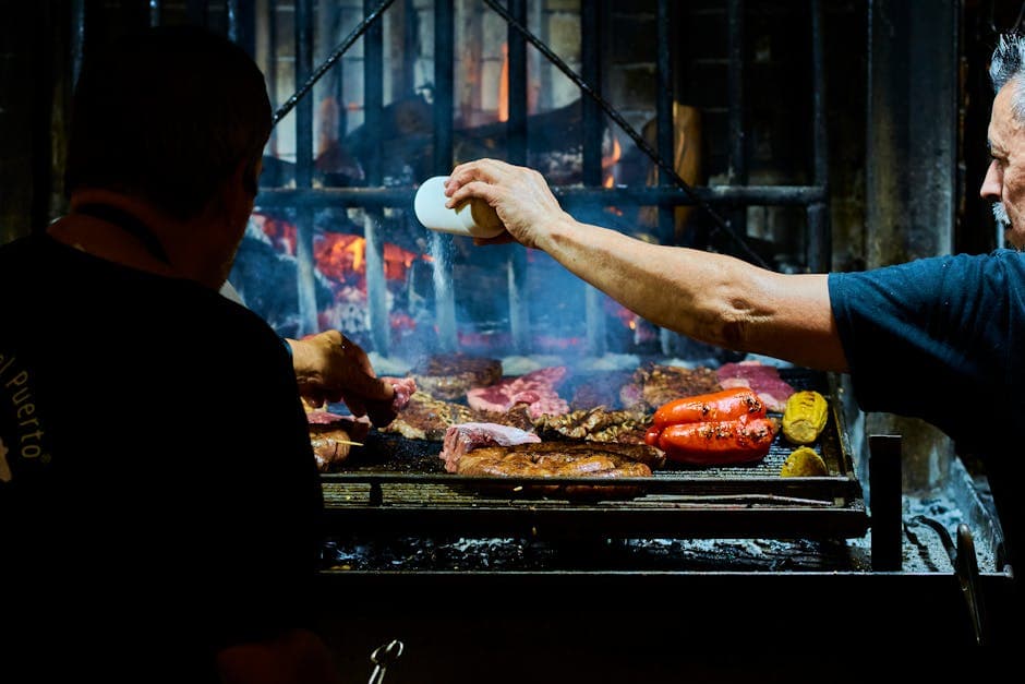 Uruguayan chefs grilling meats and vegetables over open flame in an indoor parrilla.