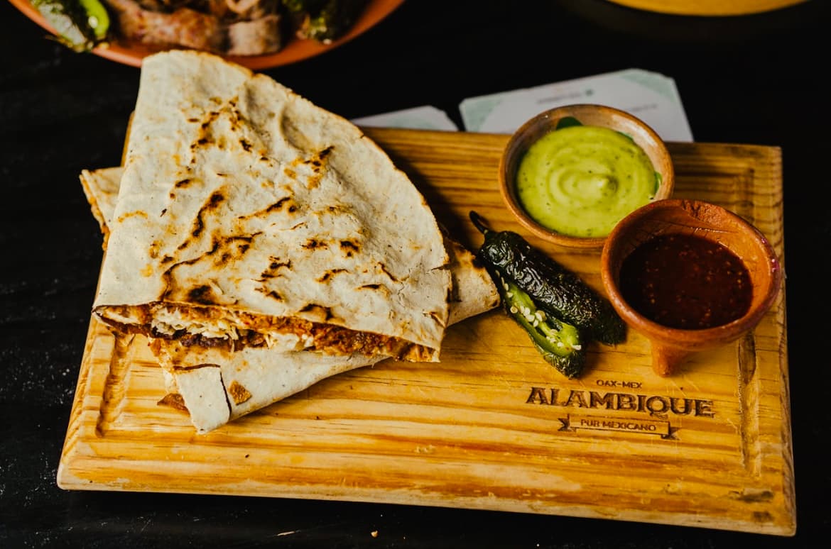 Fachada de ALAMBIQUE Oaxaca, Restobar en la calle Macedonio Alcalá 401 — muestra el letrero iluminado y la entrada con mesas al aire libre