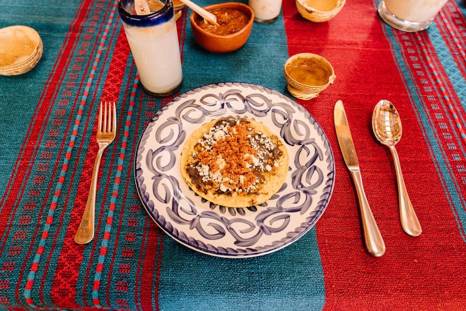 Close-up of a Mexican memela served on a vibrant woven tablecloth with silverware in Oaxaca.