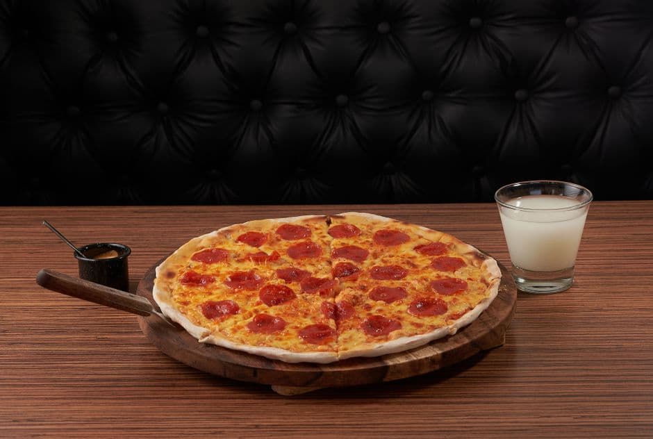 A freshly baked pepperoni pizza on a wooden table with sauce and a glass of milk.