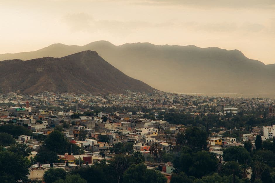 A serene aerial view of a city nestled at the base of a mountain, captured during a hazy dusk.