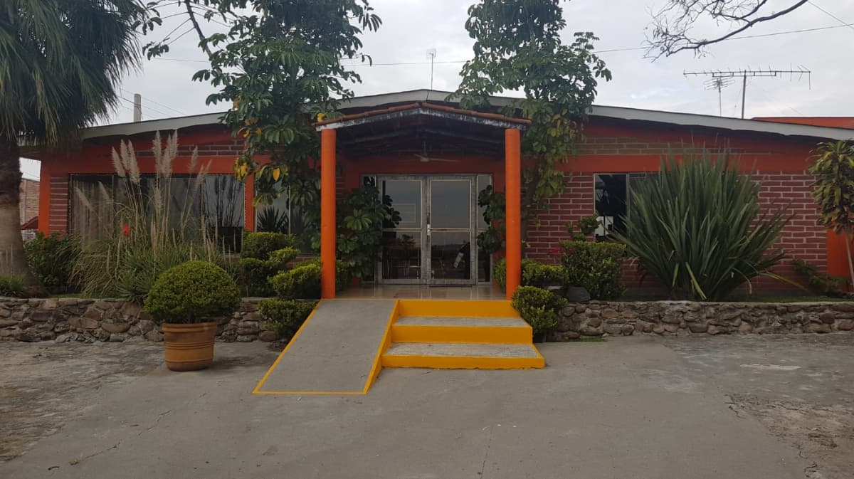 Exterior de La Cascada Restaurant con su fachada colorida y mesas al aire libre, mostrando una bandeja de tostadas con cecina al frente