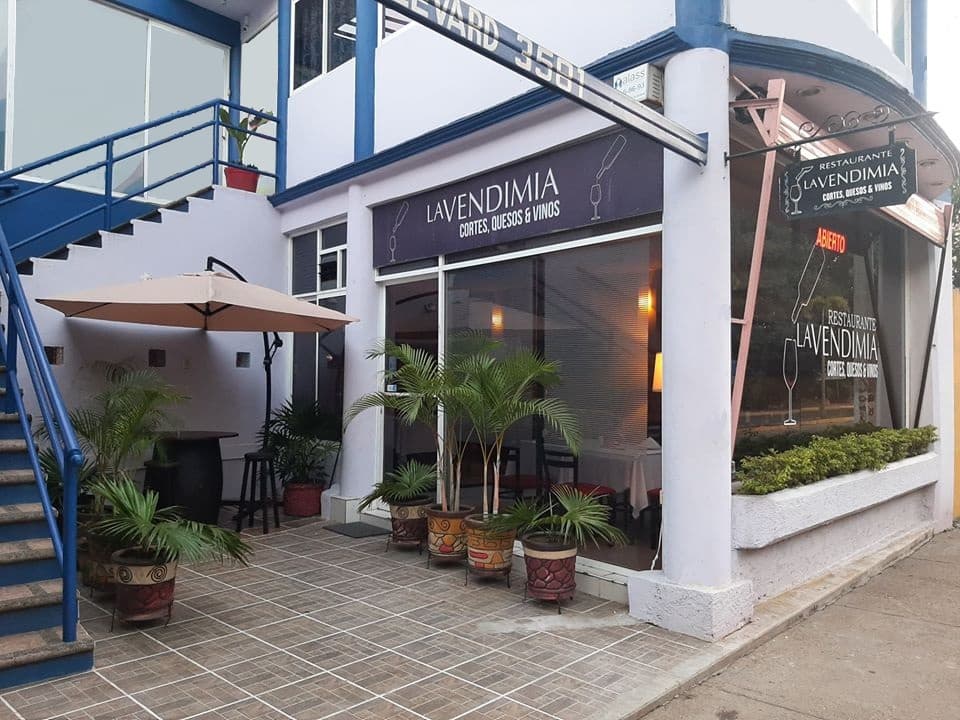 Exterior iluminado de Restaurante La Vendimia con mesas al aire libre y una botella de vino sobre la mesa