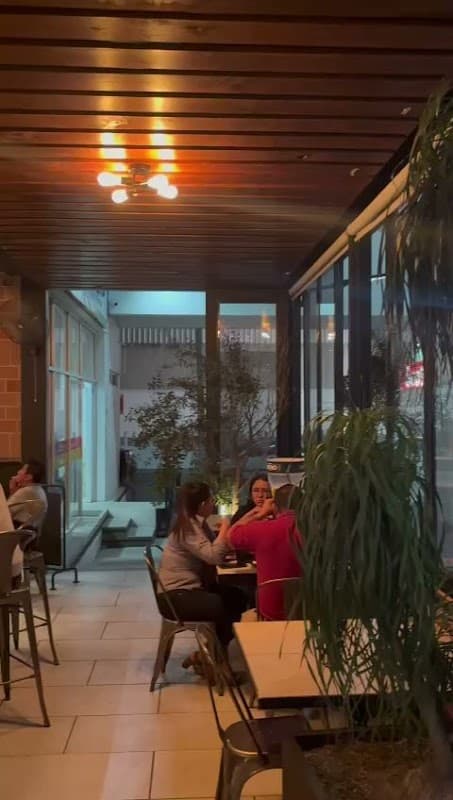 Exterior de Red Wings con su letrero iluminado y mesas al aire libre, mostrando una bandeja de alitas y una piña colada