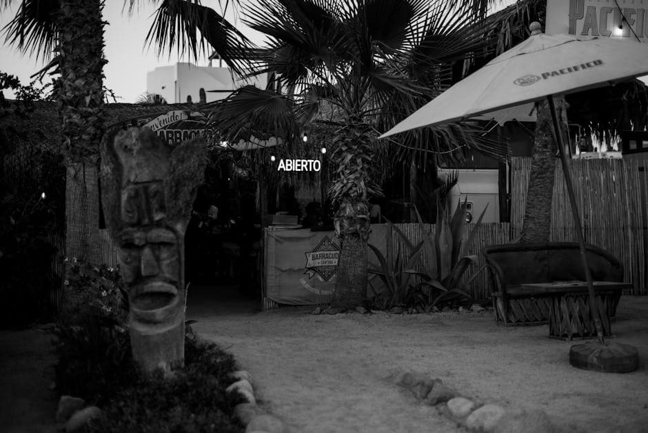 Black and white image of a beachside restaurant with tropical decor and open sign.