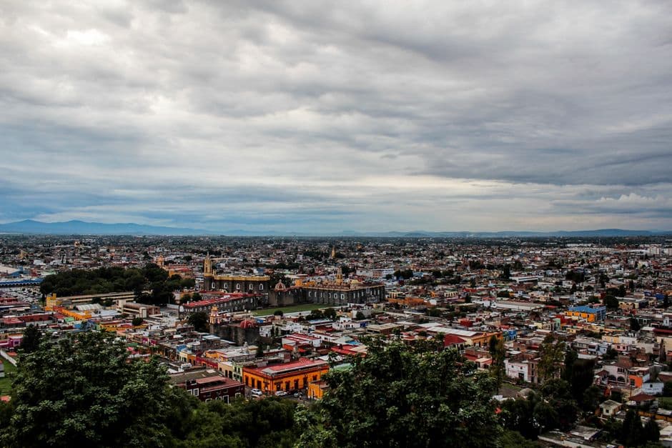 Aerial view of vibrant Cholula cityscape showcasing colorful buildings under a cloudy sky.
