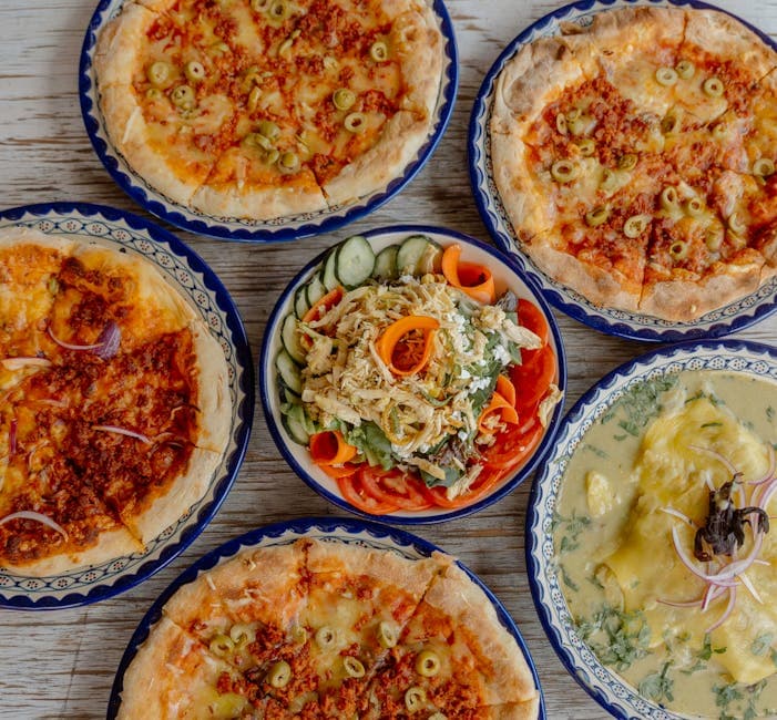 A delicious spread of pizzas and salads served on a rustic table, showcasing an appetizing meal.