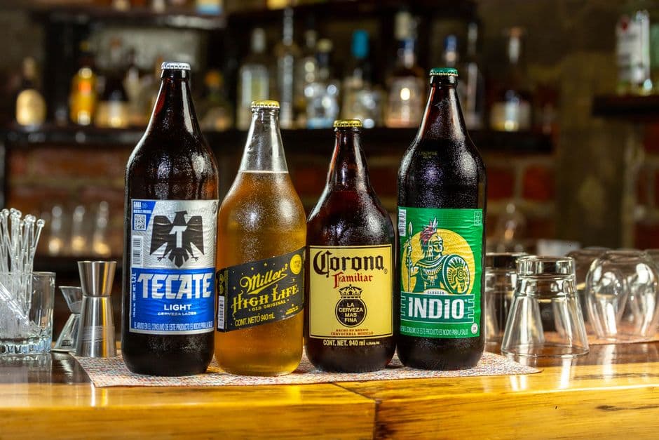 Four beer bottles including Tecate, Miller, Corona, and Indio on a bar counter.