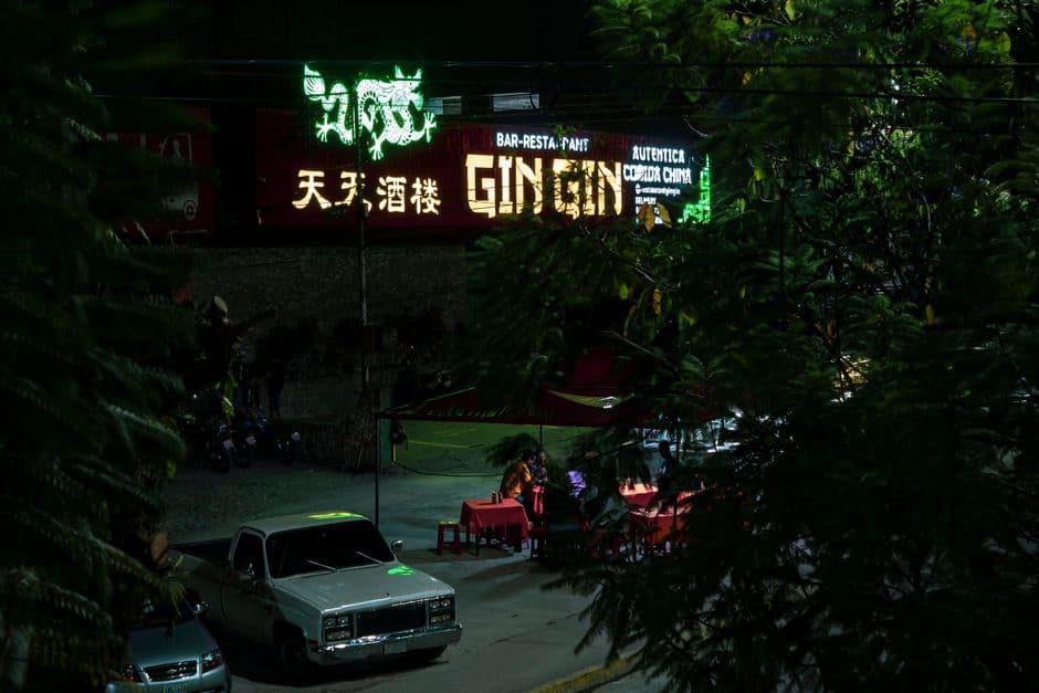 Vibrant nightlife scene in Mérida, showcasing a neon-lit street with parked cars and people enjoying dinner.
